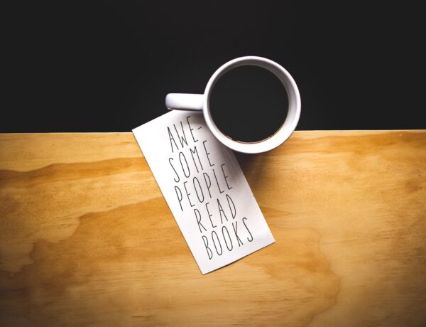 su un tavolo con una striscia di legno e una nera c'è una tazza bianca con del caffè e un pezzo di carta con la scritta "awesome people read books"