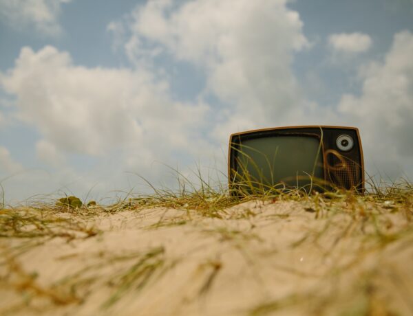 un piccolo televisore appoggiato su un campo pieno di sterpaglie. Sullo sfondo c'è il cielo con le nuvole