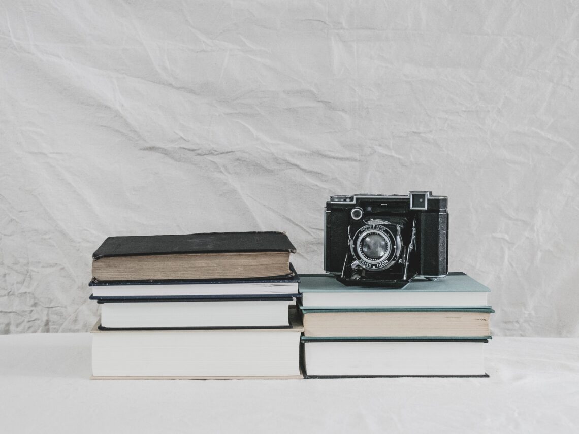 due piccole pile di libri appoggiate su un tavolo bianco. su una delle due c'è una macchina fotografica vintage
