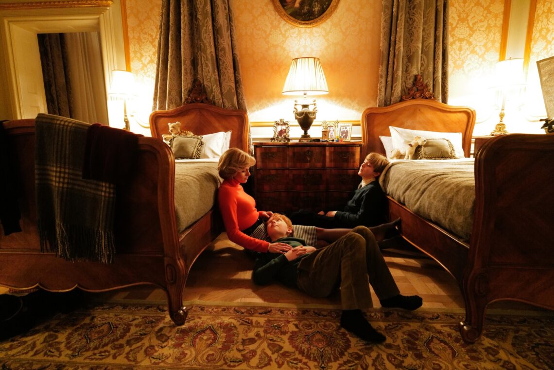 Una scena del film Spencer: Kirsten Stewart è seduta sul pavimento di una camera da letto con gli attori che interpretano William e Harry, i figli di Lady Diana